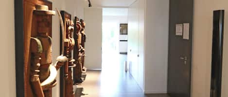 A hallway with a series of wooden sculptures on the left, a black column on the right, and a door at the end.