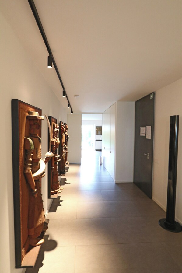 A hallway with a series of wooden sculptures on the left, a black column on the right, and a door at the end.