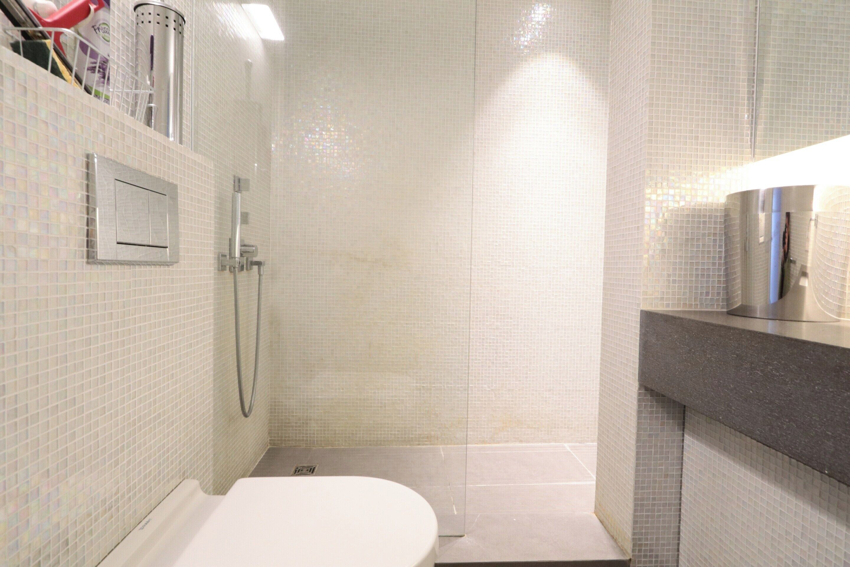Een kleine badkamer met tegels, voorzien van een douche, toilet en wastafel.
