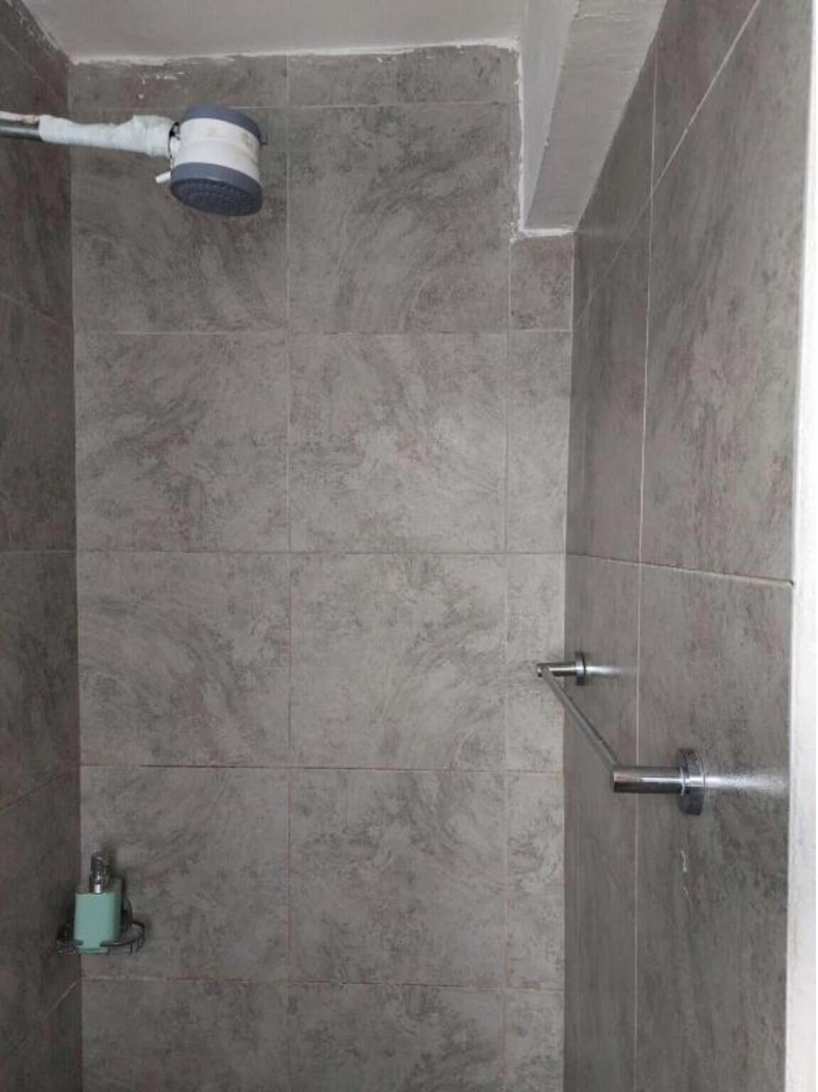 Un espacio de ducha con azulejos grises, un cabezal de ducha de mano y un grifo instalado en la pared.