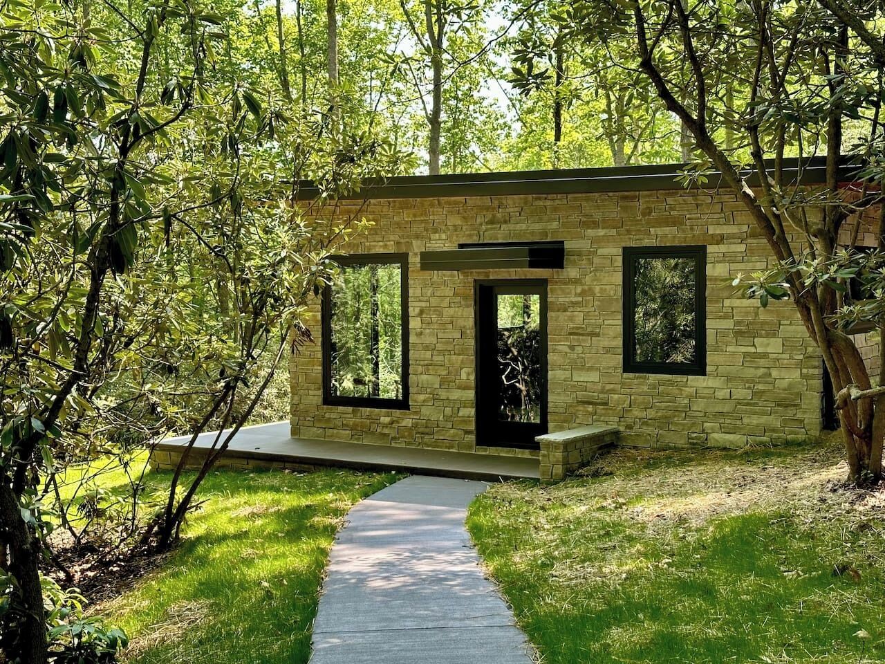 Un edifici modern de pedra amb un camí pavimentat que condueix a una porta, envoltat de vegetació exuberanta.
