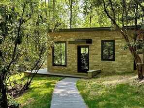 A modern stone building with a paved walkway leading to a door, surrounded by lush greenery. - Secluded Mountain Escape | River • Hot Tub • Waterfalls • Mountain Views (Marion)