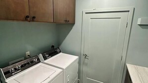 A laundry room with two white front-loading washers and dryers, wooden cabinets, a white door, and a marble countertop. - Secluded Mountain Escape | River • Hot Tub • Waterfalls • Mountain Views (Marion)