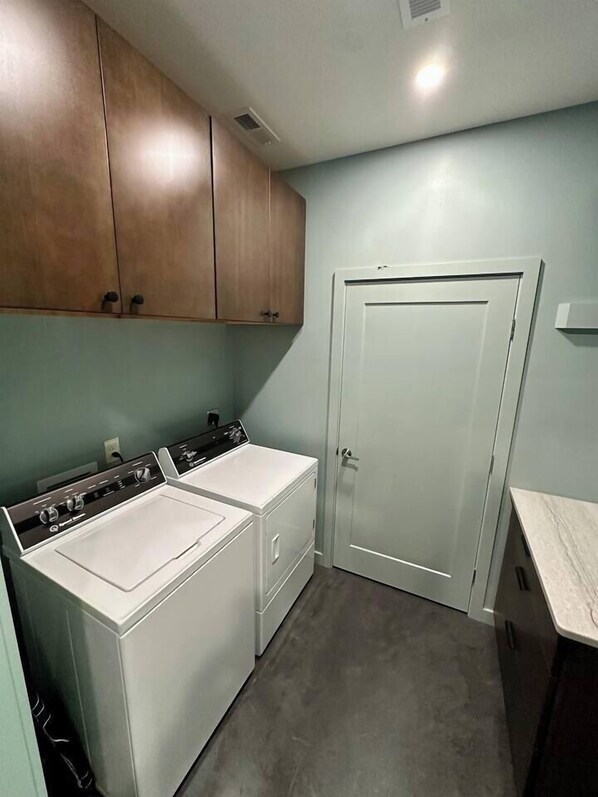 A laundry room with two white front-loading washers and dryers, wooden cabinets, a white door, and a marble countertop. - Secluded Mountain Escape | River • Hot Tub • Waterfalls • Mountain Views (Marion)