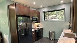 A modern kitchen with stainless steel appliances, a window with a view of greenery, and a marble countertop. - Secluded Mountain Escape | River • Hot Tub • Waterfalls • Mountain Views (Marion)