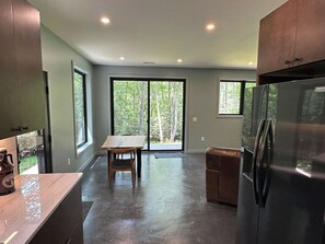 A kitchen with a large refrigerator, a dining table with chairs, and a sliding glass door leading to a deck. - Secluded Mountain Escape | River • Hot Tub • Waterfalls • Mountain Views (Marion)