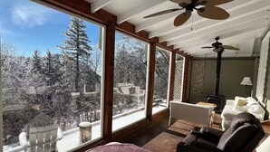 A room with large windows, a ceiling fan, a fireplace, and a sofa.