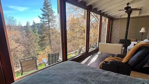 A bedroom with a large window, a bed, a chair, and a ceiling fan.