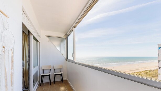 Uma varanda com vista para a praia, duas cadeiras e um ventilador.