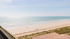Vista da praia a partir de um edifício com telhado em cerâmica e uma praia arenosa em primeiro plano.