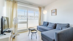 Uma sala de estar moderna com um sofá cinzento, uma mesinha redonda, uma TV e um ventilador.