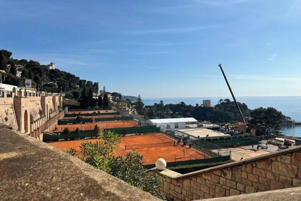 Vista costera con cancha de tenis, un edificio histórico y cielo despejado.