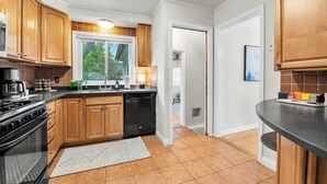 A kitchen with wooden cabinets, a black stove, and a dishwasher. - Elegant, Artsy Home in N. Royal Oak! (Royal Oak)