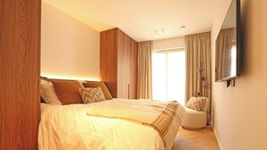 A modern bedroom with a large bed, a bedside table, a chair, and a large mirror on the wall. - Apartment in Het Zoute Near the Beach (Knokke-Heist)