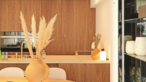 A modern kitchen with wooden cabinets, a dining area with a round table and chairs, and a glass display cabinet. - Apartment in Het Zoute Near the Beach (Knokke-Heist)