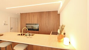 A modern kitchen with a wooden panel wall, a stainless steel oven, a sink with a gold faucet, and bar stools. - Apartment in Het Zoute Near the Beach (Knokke-Heist)