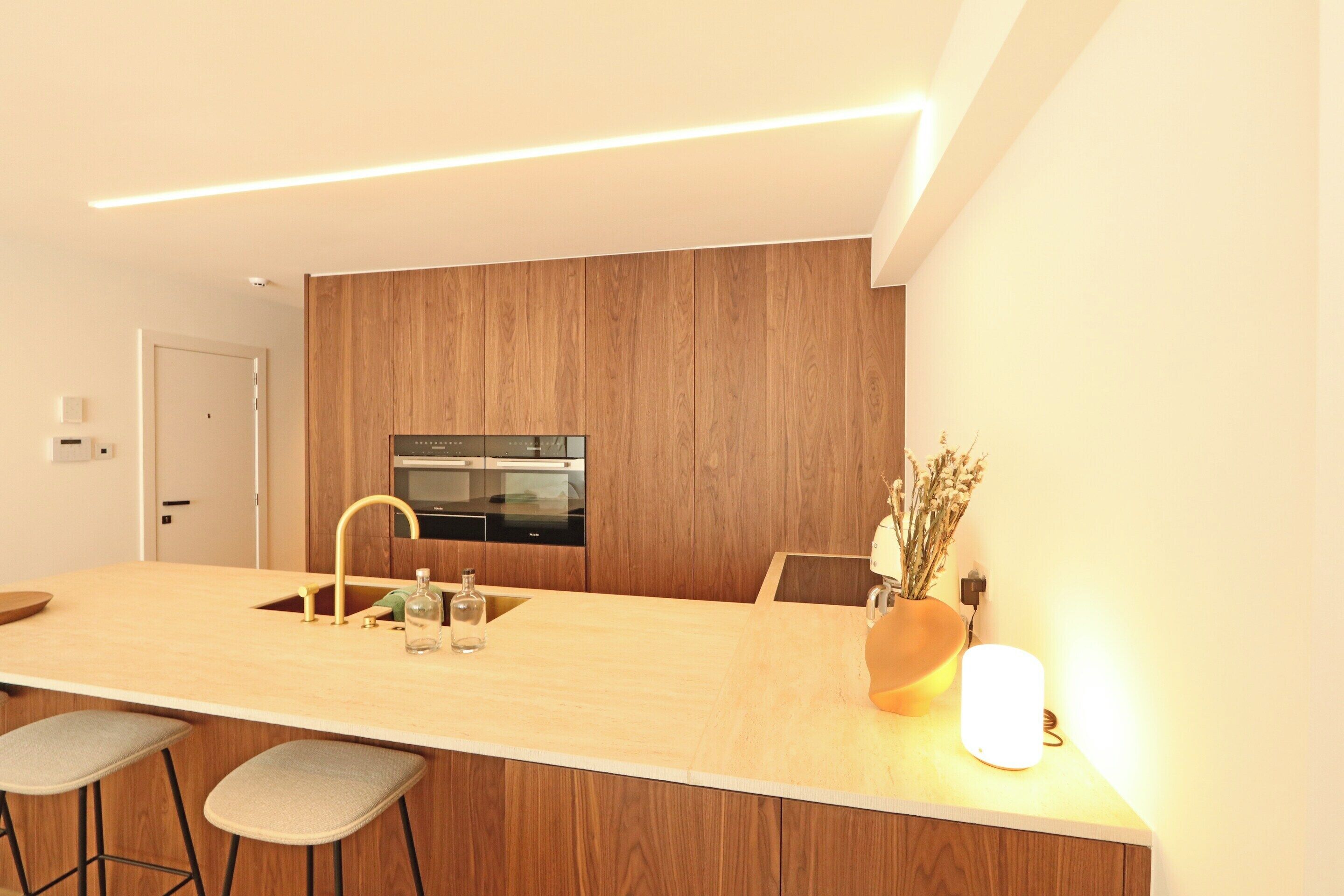 A modern kitchen with a wooden panel wall, a built-in oven, and a bar area with stools.