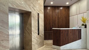 A modern reception area with a marble floor, a wooden reception desk, and a vertical wooden panel wall. - Ocean Vista Marina Suites Nha Trang (Nha Trang)