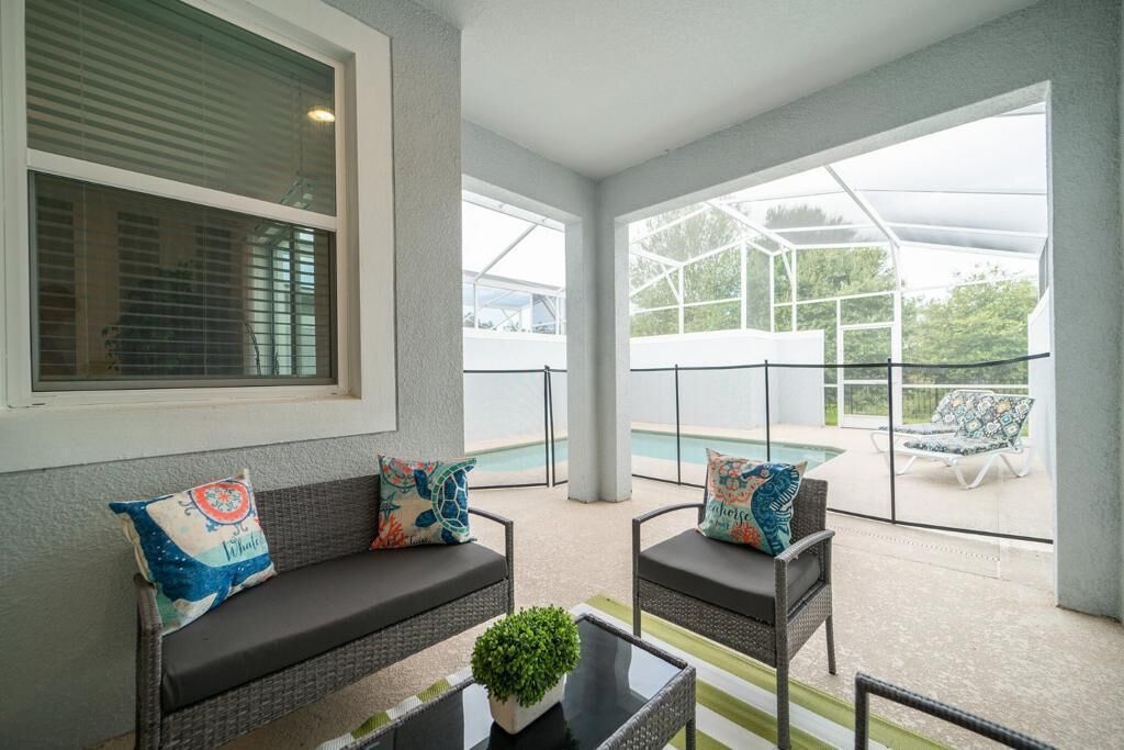 A covered outdoor seating area with a pool in the background.