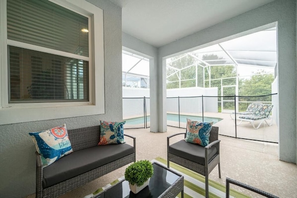 A covered outdoor seating area with a pool in the background.