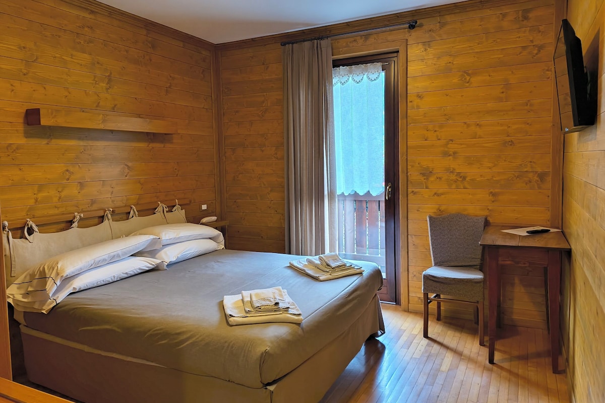 Una habitación con paneles de madera, con una cama, una silla, una mesa y un televisor.