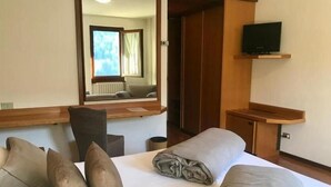 A hotel room with a bed, a desk, a chair, a television, and a mirror. - Hotel Sorriso  (Temu)