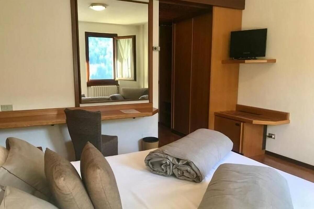 A hotel room with a bed, a desk, a chair, a television, and a mirror.