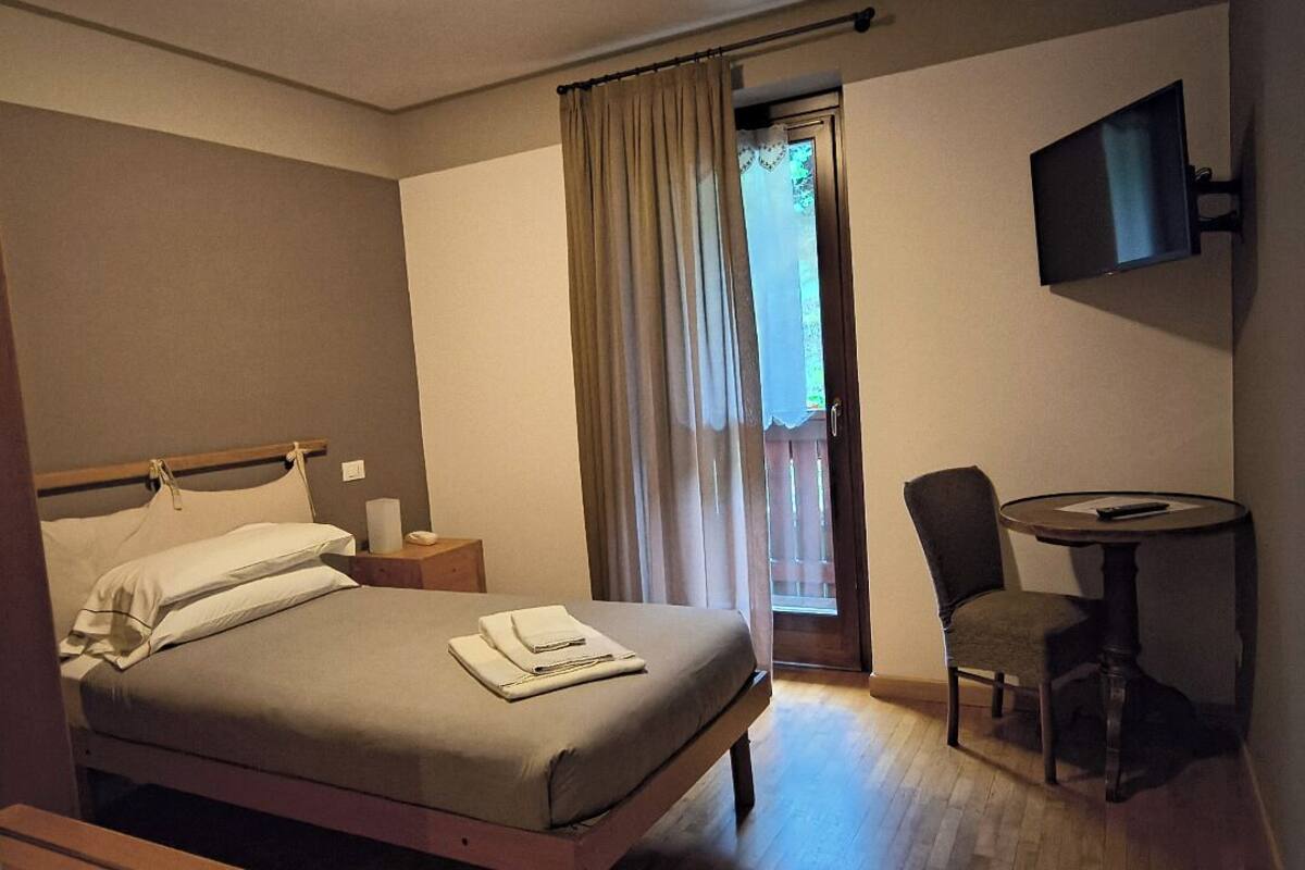 A hotel room with a bed, bedside table, chair, and a TV mounted on the wall.