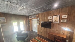 A room with a wooden wall, a flat-screen TV, a bench, a desk, and a chair. - 1st Floor 2BR Downtown + 2 Parking Spaces (Elkader)