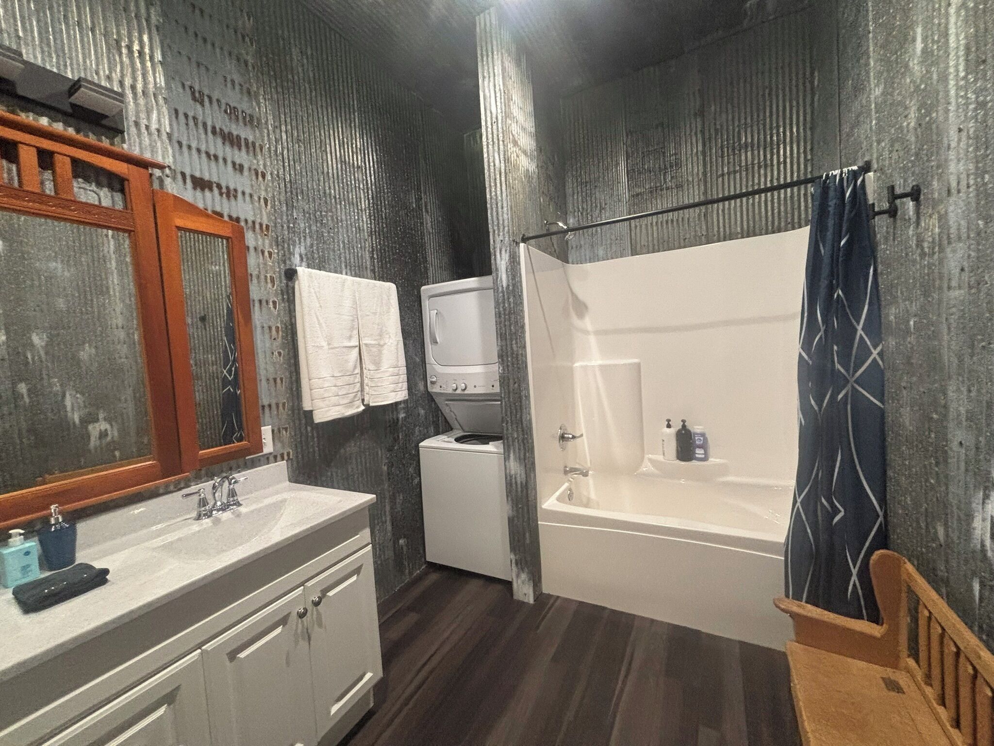 Ein Badezimmer mit einem Holzkosmetikschrank, einem weißen Waschbecken, einem Spiegel, einer weißen Toilette, einer Badewanne und einer Duschvorhang.