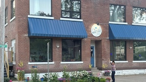 A brick building with large windows and a blue awning, labeled "Bridge Street Suites." - 1st Floor 2BR Downtown + 2 Parking Spaces (Elkader)