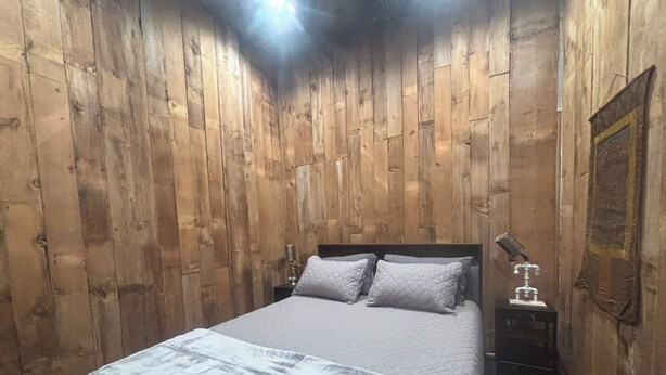 Een kamer met houten lambrisering, een bed, nachtkastje en een wandlamp.