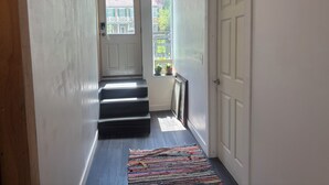 A narrow hallway with a wooden floor, a black carpet, and a white door at the end. - 1st Floor 2BR Downtown + 2 Parking Spaces (Elkader)