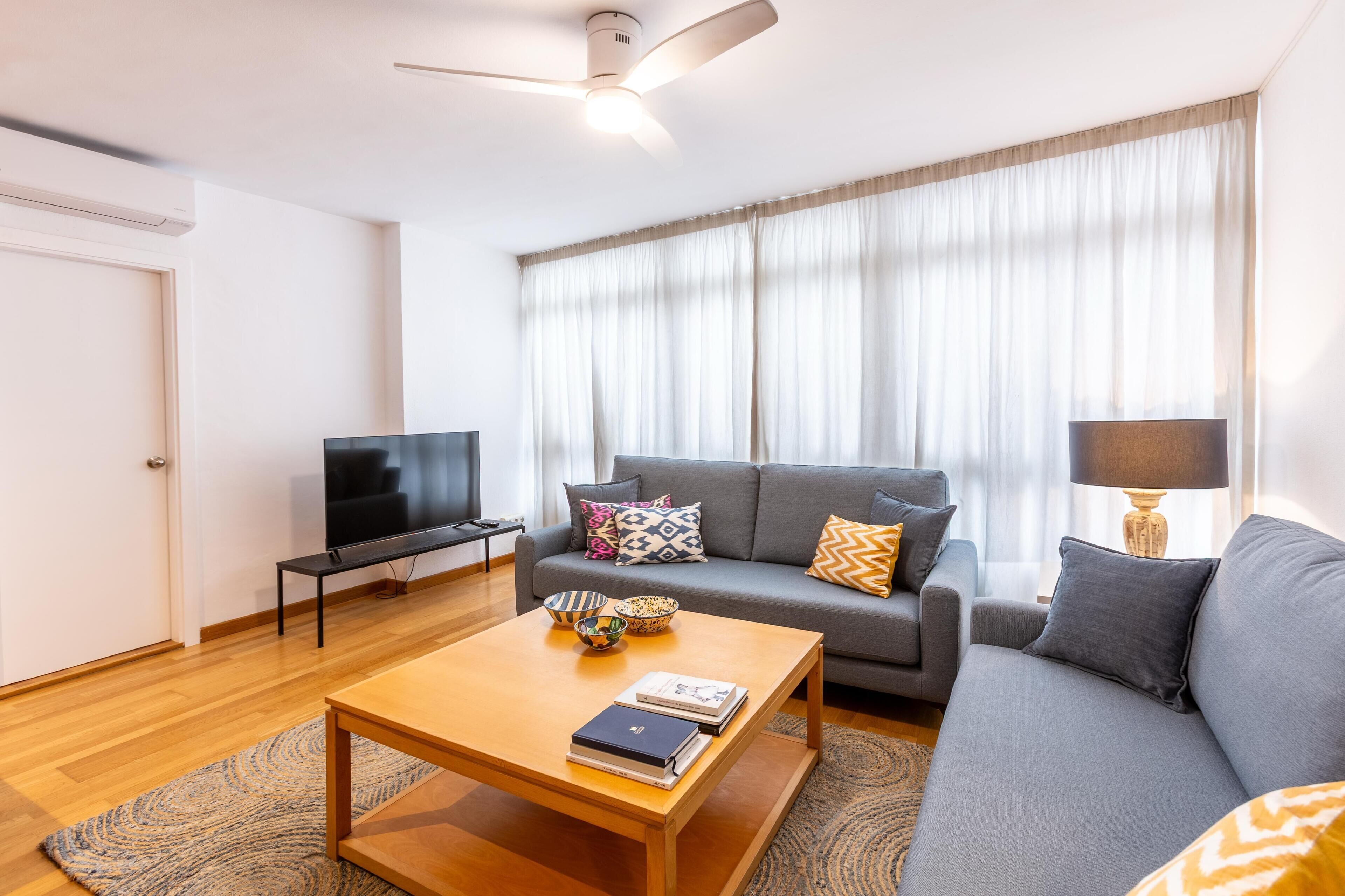 A modern living room with a grey sofa, a wooden coffee table, a TV, and a ceiling fan.