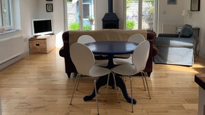 A spacious living room with a high ceiling, a dining area with a round table and chairs, a fireplace, and large windows allowing natural light.