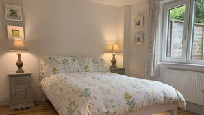 A bedroom with a floral bedspread, two bedside lamps, a nightstand, and a window with curtains.
