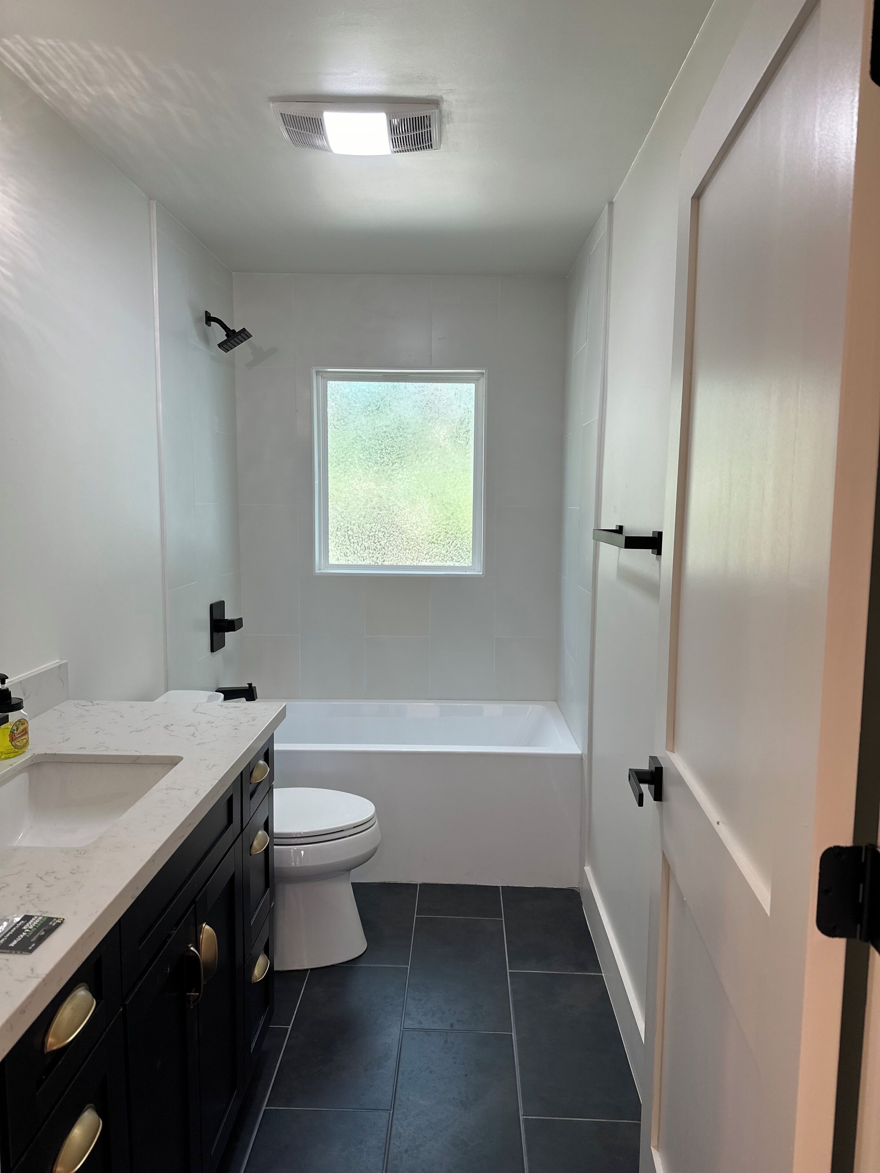 Ein modernes Badezimmer mit Toilette, Badewanne, Fenster und Waschbecken.