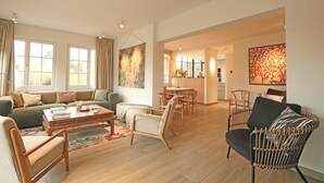 A spacious living room with a sofa, coffee table, and chairs, a dining area with a table and chairs, and a kitchen in the background. - Villa in Het Zoute Near Zeedijk Promenade (Knokke-Heist)