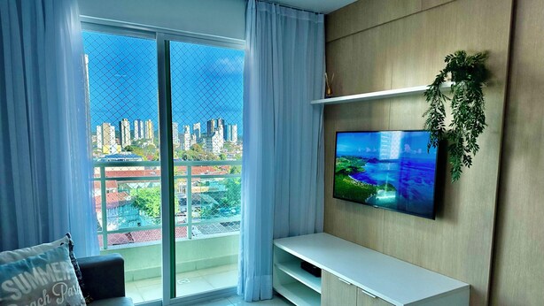 A modern living room with a large TV, a sofa, and a balcony with a city view.