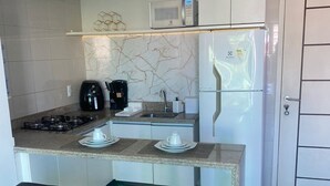 A modern kitchen with a gas stove, a coffee maker, and a refrigerator. There are two bar stools in front of the counter.