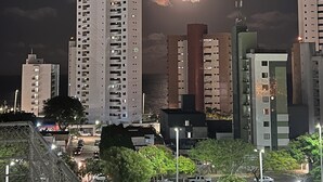 A nighttime cityscape with high-rise buildings, a bridge, and a park area with people and vehicles.