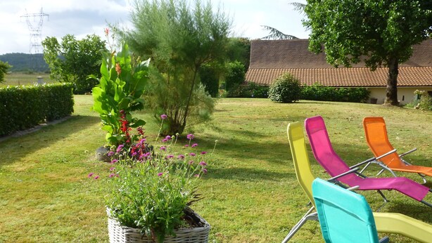 A garden with a wicker planter, colorful chairs, and a building with a tiled roof. - Purple perigord house (Lanquais)