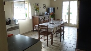 A kitchen with a dining table, chairs, a TV, and a window with curtains. - Purple perigord house (Lanquais)