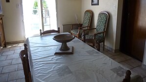 A dining area with a table set for two, two chairs, a wooden cabinet, and a door leading outside. - Purple perigord house (Lanquais)
