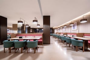 Un ristorante moderno con banquette e tavoli, caratterizzato da lampade a sospensione e un design pulito e minimalista.