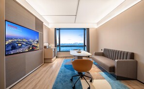 A modern hotel room with a large TV displaying a cityscape, a comfortable sofa, a small table, and a view of the city through large windows. - Intercity Hotel Shanghai Hongqiao Airport (Shanghai)