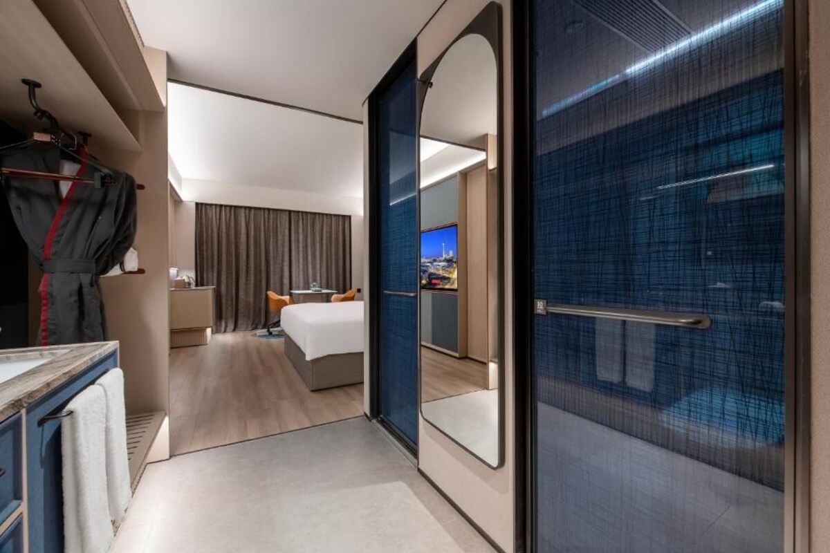 A modern hotel room with a bed, bedside table, and a large mirror.