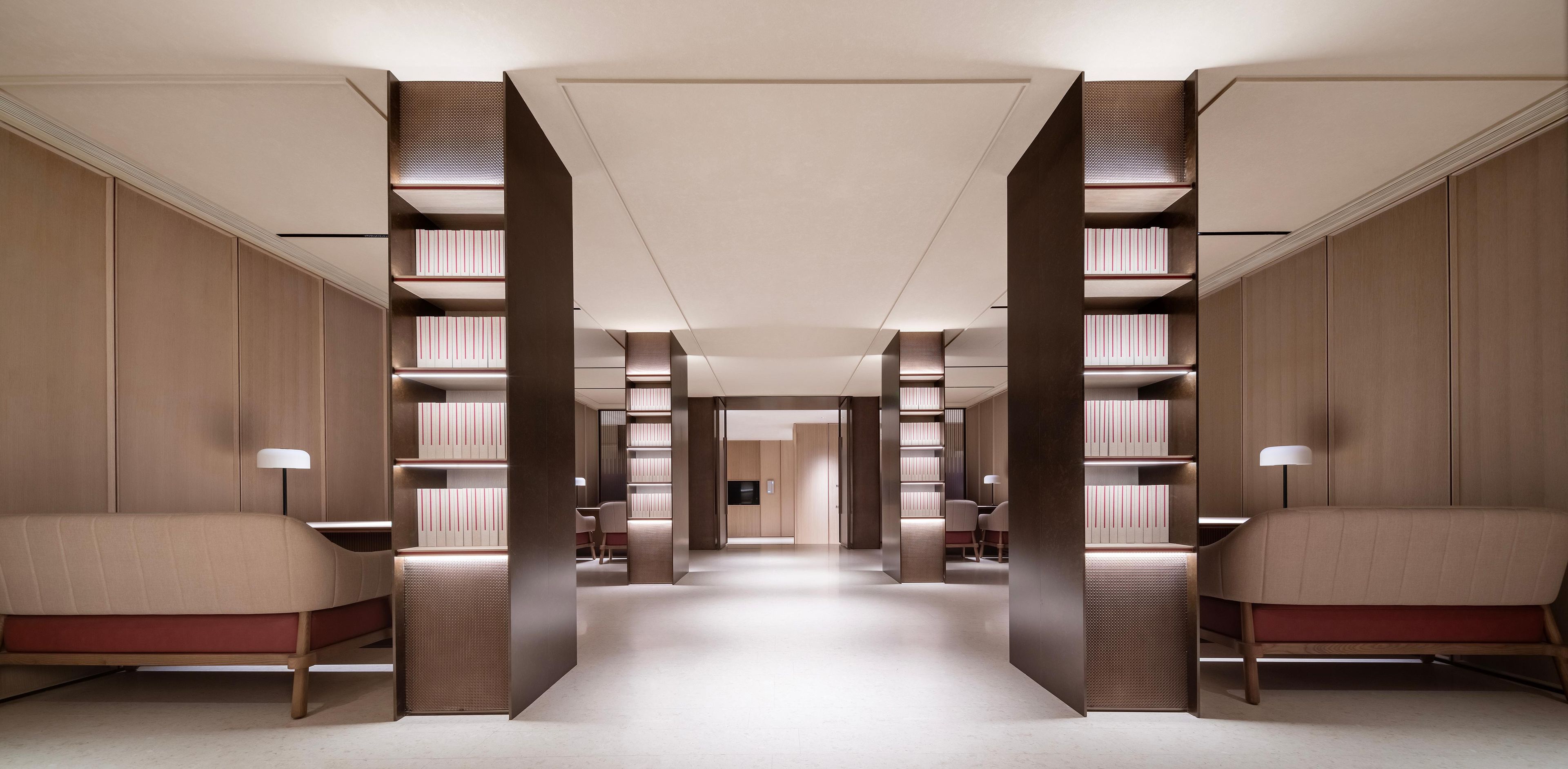 A modern hotel lobby with a central walkway, wooden paneling, and bookshelves on either side.