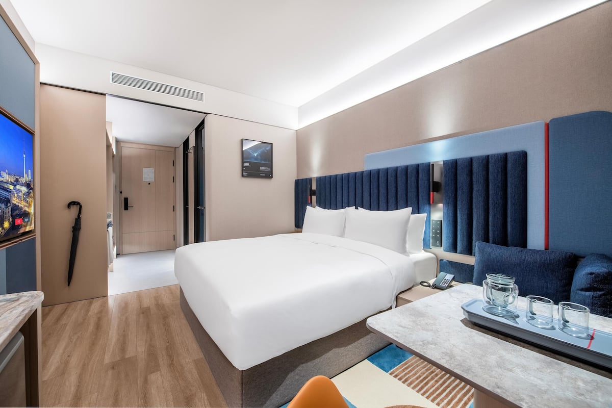 Ein modernes Hotelzimmer mit einem großen Bett, einem Schreibtisch mit Telefon und Brille sowie einem Fernseher links.