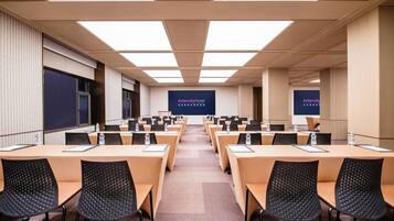Un salón de conferencias con varias mesas y sillas, una pantalla grande mostrando la marca 'Intercity Hotel' y un diseño de techo moderno.